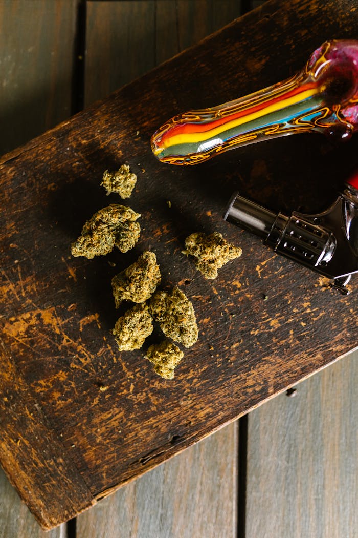 A colorful glass pipe and cannabis buds placed on a rustic wooden table in a vertical shot.